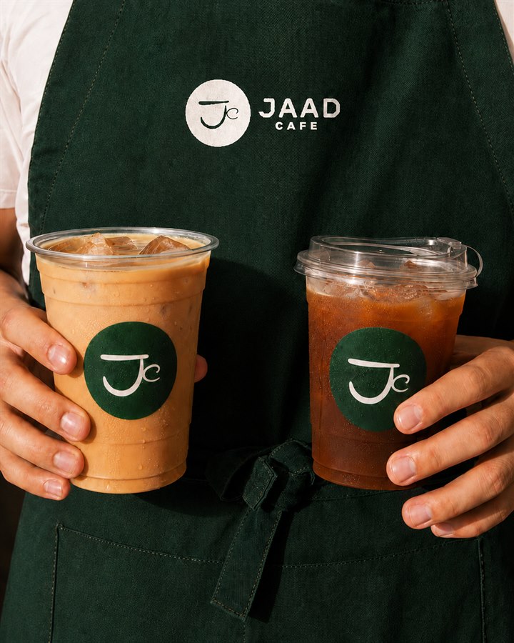 Barista Jaad Cafe dengan apron memegang dua es kopi